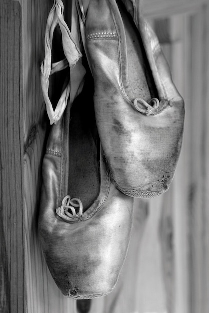 Photo worn out ballet pointe shoes hanging by the satin ribbons. black and white.