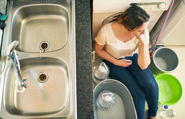 Foto preoccupato per l'acqua inquadratura dall'alto di una bella giovane donna che si sente depressa per la crisi idrica mentre è seduta sul pavimento in cucina a casa