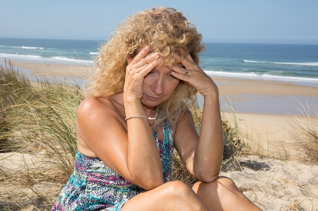 Foto ragazza bionda preoccupata sulla spiaggia che si siede sulla sabbia