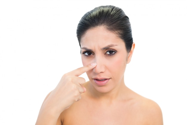 Worried brunette pointing to nose and looking at camera