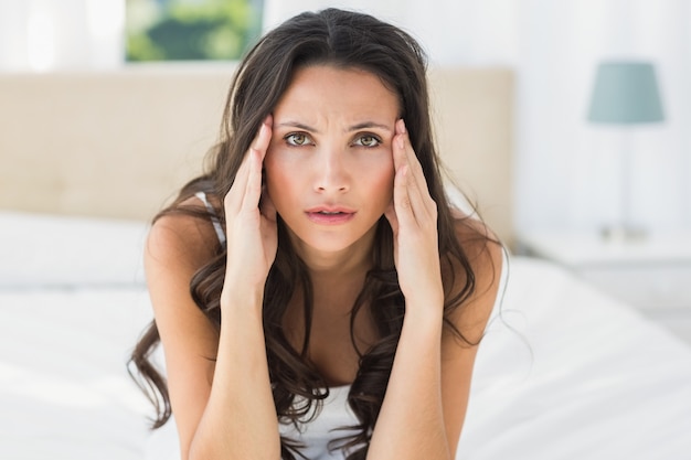 Worried brunette sitting on bed at home in bedroom