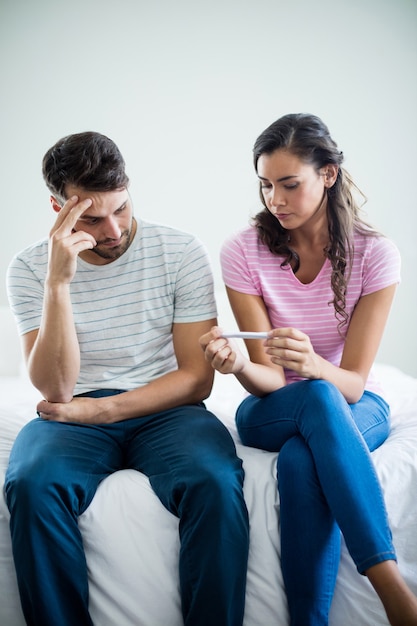 Foto coppia preoccupata che scopre i risultati di un test di gravidanza in camera da letto a casa