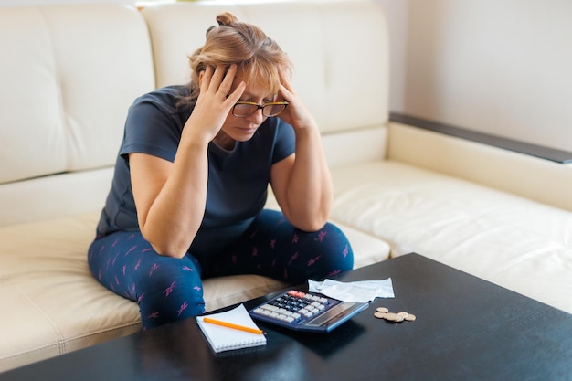 Foto donna caucasica preoccupata e disperata che calcola le spese monetarie domestiche facendo scartoffie e fatture bancarie contabili con calcolatrice che soffre di stress in problemi finanziari e depressione