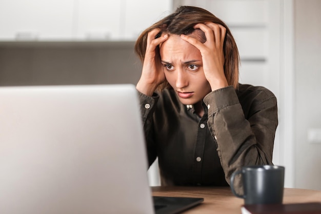 Foto ragazza preoccupata seduta al tavolo e guardando lo schermo del laptop che le tocca la testa