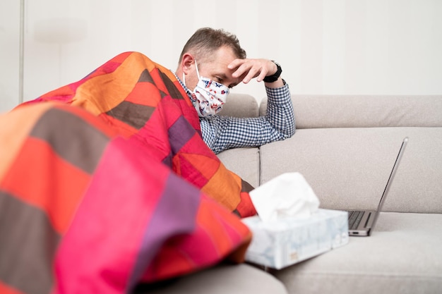 Foto uomo preoccupato e malato a casa ritratto di un malato che indossa maschere mediche utilizzando il laptop durante il virus