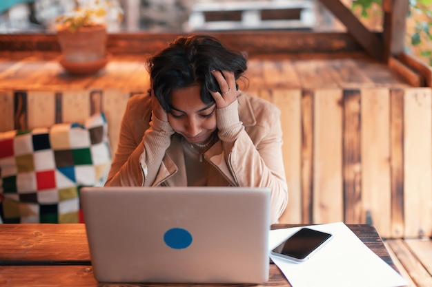 Photo worried indian girl with hands in her hair sitting in front of laptop