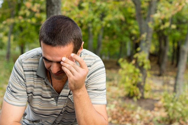 Worried man sitting alone outdoors with his hand raise to his forehead