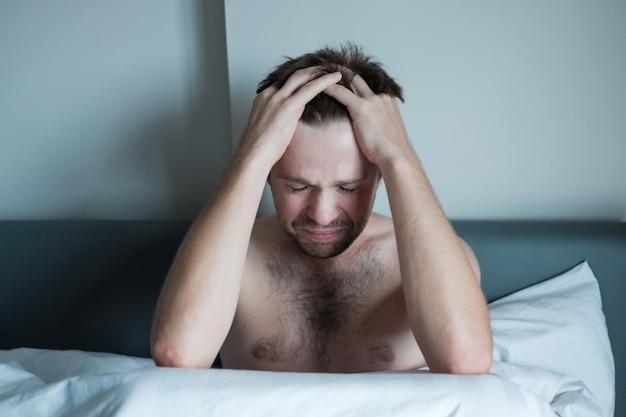 Worried man sitting on bed with hand on forehead He has problem with mental health and hear voices in his head