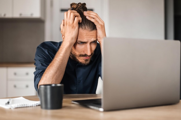 Uomo preoccupato seduto al tavolo e guardando lo schermo del laptop