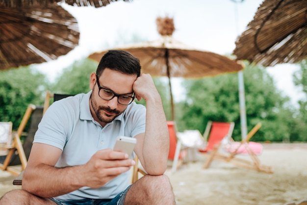 Uomo preoccupato che per mezzo del telefono mentre sedendosi su una spiaggia.