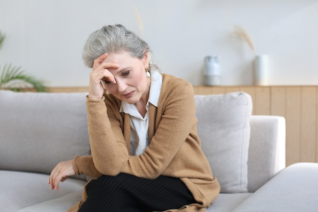 worried middle aged woman sitting on a sofa in the living room.
