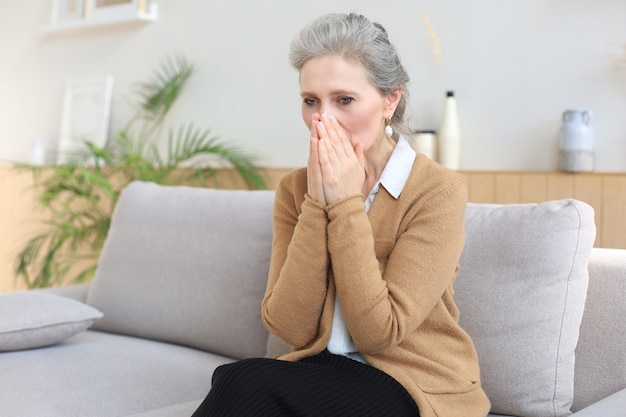 Worried middle aged woman sitting on a sofa in the living room.