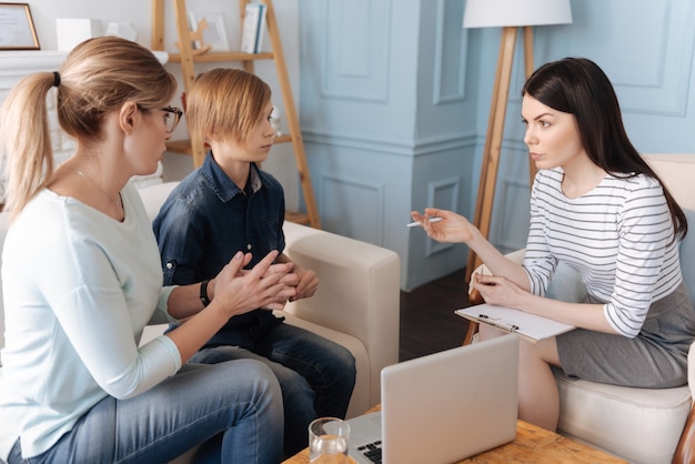 Worried mummy wearing casual clothes keeping her hair in ponytail sitting in semi position next to her son