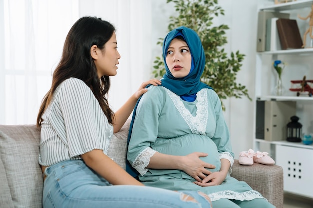 걱정하는 이슬람 임산부는 집 거실에서 아시아 한국 친구로부터 스트레스와 지원을 받습니다. 우울한 젊은 산모는 자매의 이야기를 듣고 그녀를 위로하기 위해 이야기합니다.