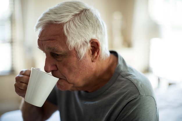 Uomo maggiore preoccupato che mangia caffè nero in camera da letto a casa