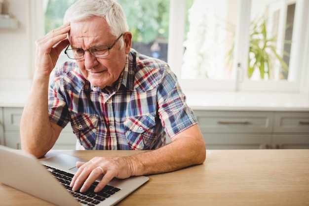 Uomo senior preoccupato che per mezzo del computer portatile a casa