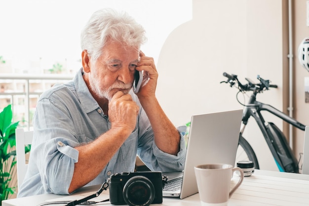 Worried senior man using mobile phone sitting outdoor on home terrace using modern technology