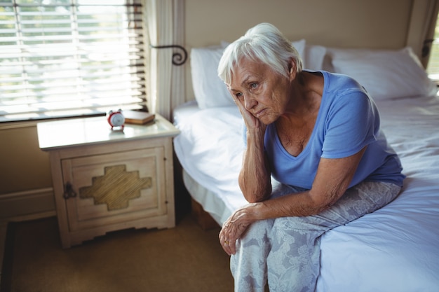 Worried senior woman sitting on bed in the bedroom at home