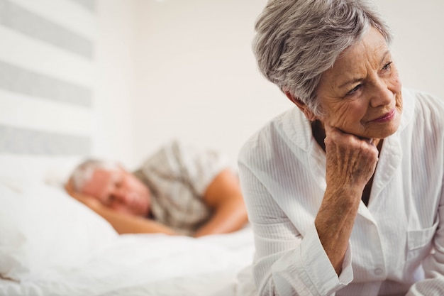 Worried senior woman sitting on bed in bedroom