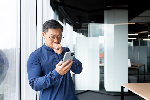 A worried and serious young asian man is standing in the lobby of an office hospital bank holds the