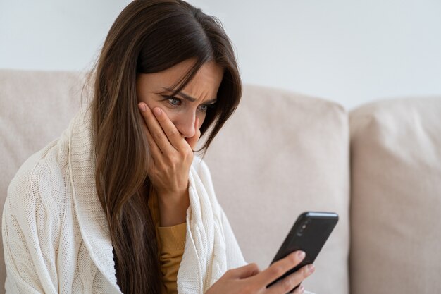 Worried woman holds mobile phone read message unpleasant sms