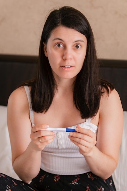 worried woman with positive pregnancy test in bed