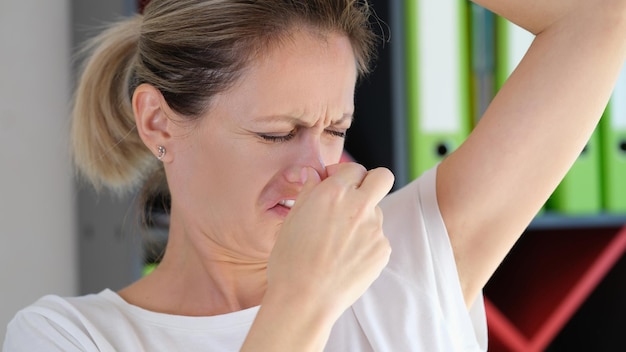 Обеспокоенная женщина с несчастным лицом проверяет запах своей подмышки в офисе, плохой запах тела и здоровье