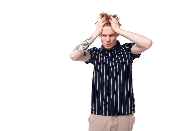 Worried young blond guy in a striped polo shirt with a tattoo on a white background
