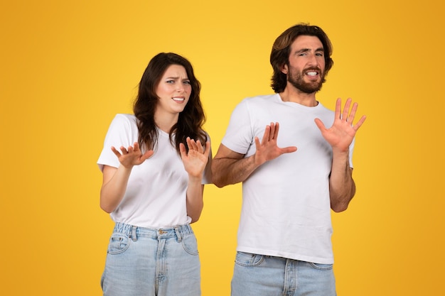 Worried young couple gesturing stop with their hands showing signs of rejection or fear