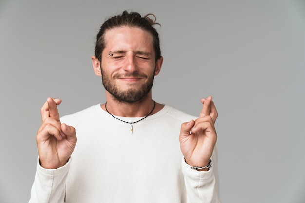 灰色で孤立して立って、幸運のために指を交差させて保持している心配している若い男