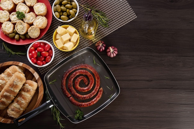 Worst en lookbrood op een rode plaat op de barbecuetafel met hapjes, kaas, rozemarijn, olijven en kerstomaatjes. Bovenaanzicht.