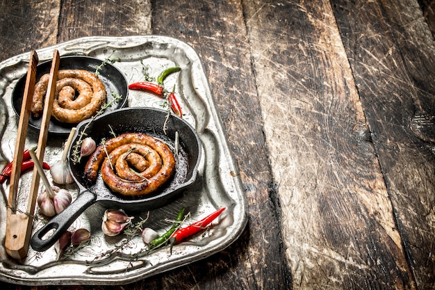 Worsten in pannen op stalen dienblad met hete chilipepers op houten tafel.