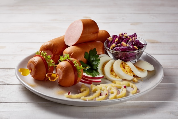 Worsten met groenten en kruiden garneren met sauzen en brood op een grijze keramische plaat op een witte houten tafel.