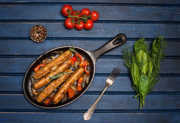 Worsten op de grillpan op blauwe achtergrond Koekenpan met gebakken worsttomatenkruiden