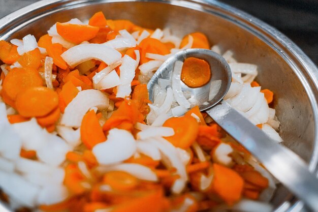 Wortelen en uien worden gestoofd in een groot glanzend bord op het fornuis Groenten worden klaargemaakt om te eten