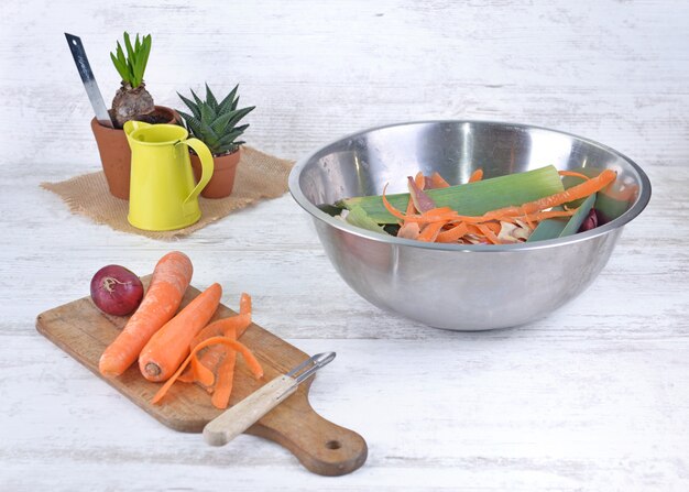 Wortelen pellen op een koken plank en kom vol afval op een tafel in een keuken