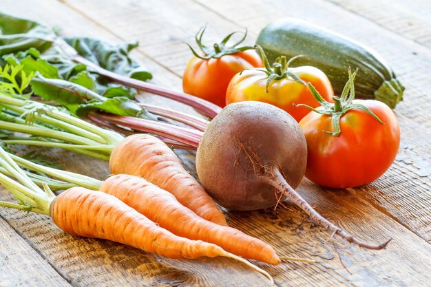 Wortelen, rode biet, tomaten en courgette net geplukt in de tuin op houten planken