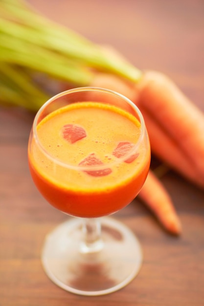 Wortelsap groente en gezond eten of drinken met kleurkunst en voedingsdeskundige creativiteit Veganistische smoothie of oranje vloeistof in glas voor wellnessdieet of voeding op een houten tafel met ijs