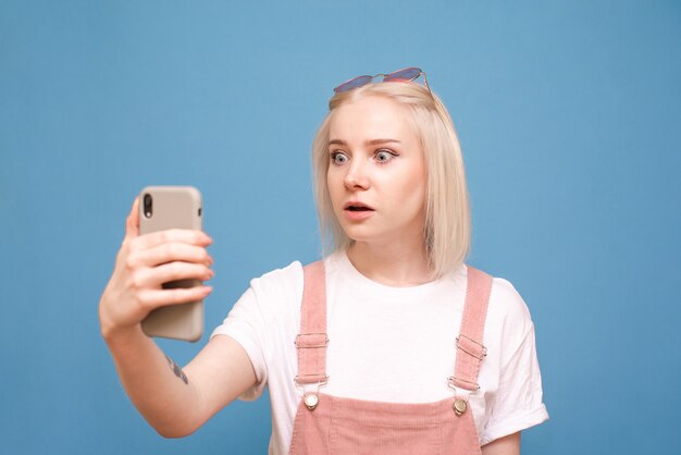 woteenager met een smartphone in haar hand, met een verbaasd gezicht kijkend naar het scherm van een telefoon op blauw