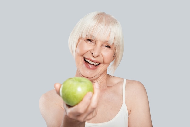 Would you like some? Beautiful senior woman holding an apple and smiling 