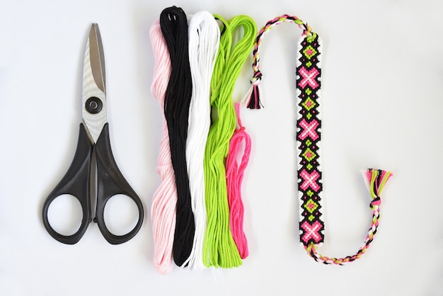 Woven handmade friendship bracelet with skeins of thread and scissors on white background