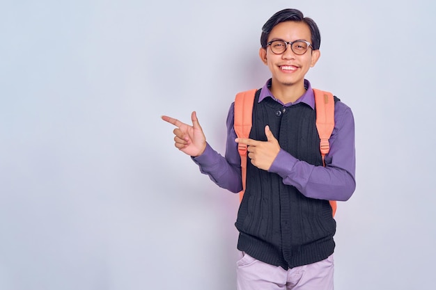 Wow attention to advertising Portrait of happy Asian Student man pointing to side copy space isolated on gray background Education in high school university college concept