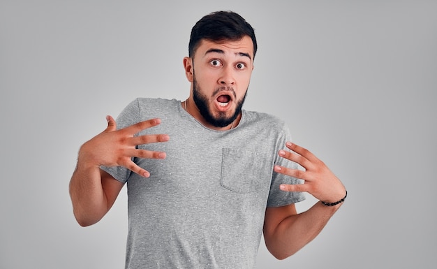 Wow. Attractive male half-length front portrait on gray studio backgroud. Young emotional surprised bearded man standing with open mouth. Human emotions, facial expression concept.