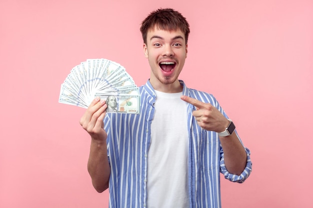 Wow big money Portrait of excited amazed brunette man with small beard and mustache in casual shirt pointing at money looking at camera with open mouth astonished face indoor isolated on pink