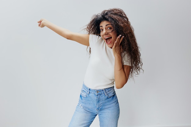 Wow concept shocked pretty curly latin woman close mouth look\
at camera and point finger up autumn collection seasonal sale\
clothing fashion brands studio shoot copy space white\
background