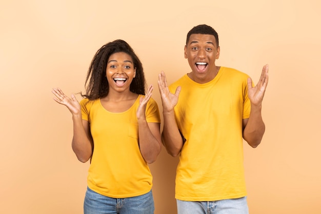 Wow Excited african american couple gesturing in amazement and looking at camera with open mouths peach background