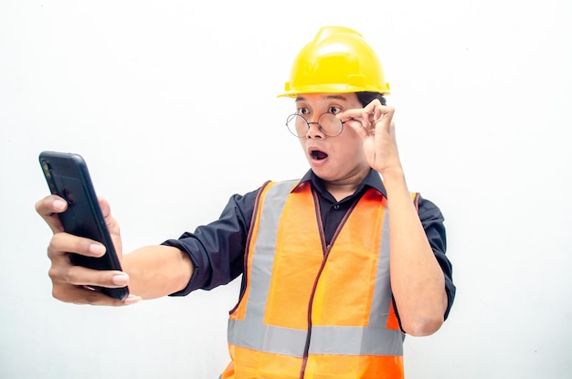 wow excited asian male construction worker in orange vest and yellow safety hardhat holding phone