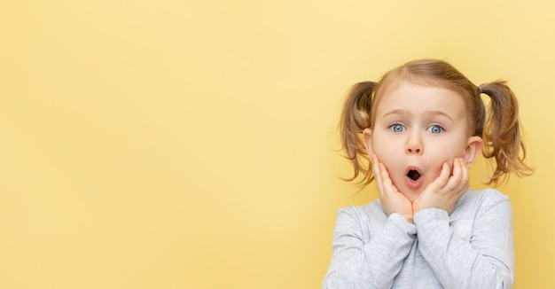 うわー興奮した子供は黄色の孤立した壁を越えて彼女の頬に触れています