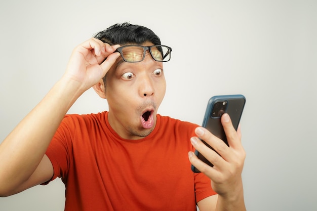 Wow face of Asian man in orange tshirt shocked what he see in the smartphone on isolated background