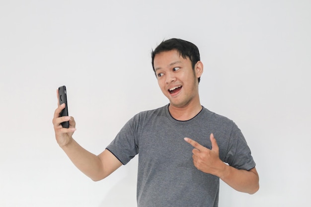 すごい顔と灰色のTシャツを着た若いアジア人の幸せな気持ちがスマートフォンで驚かされる